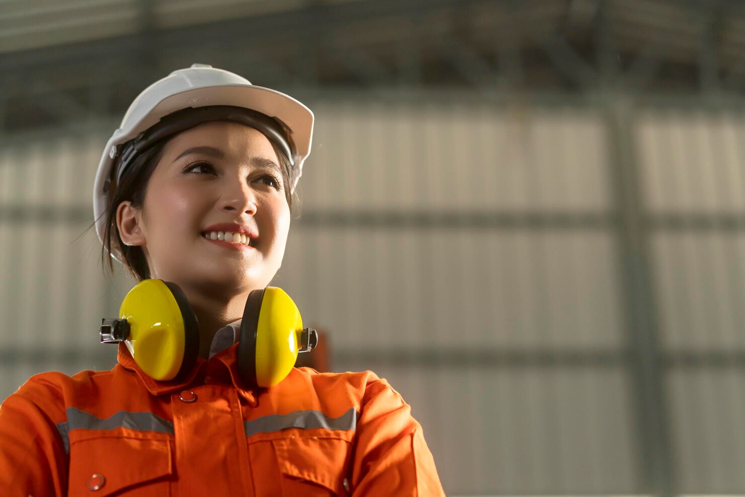 A worker in a hard hat, ear defenders and orange coveralls on site